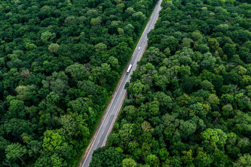 Photo aérienne d'un camion roulant sur une route au milieu d'une forêt